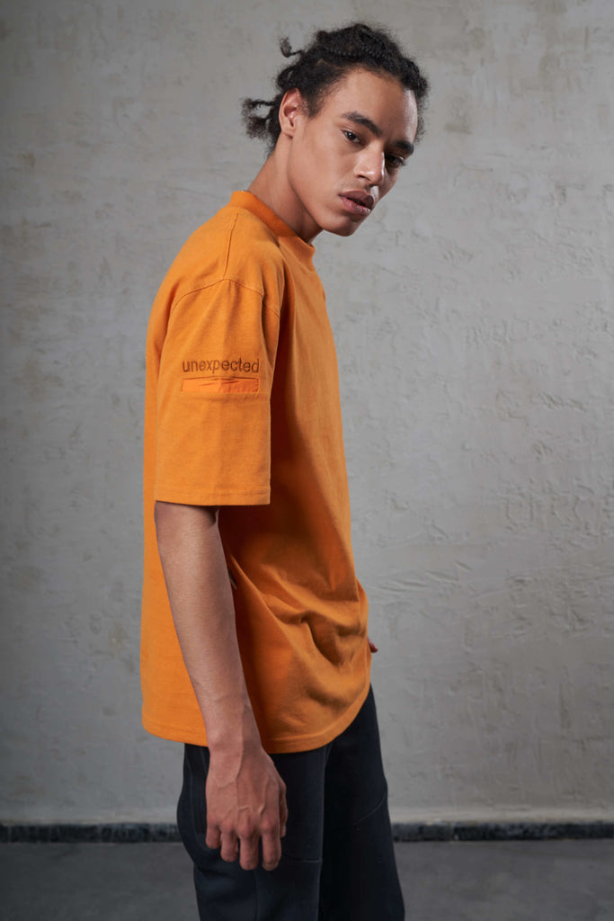 side of an orange sustainable cotton t-shirt on a young black man with pocket on arm